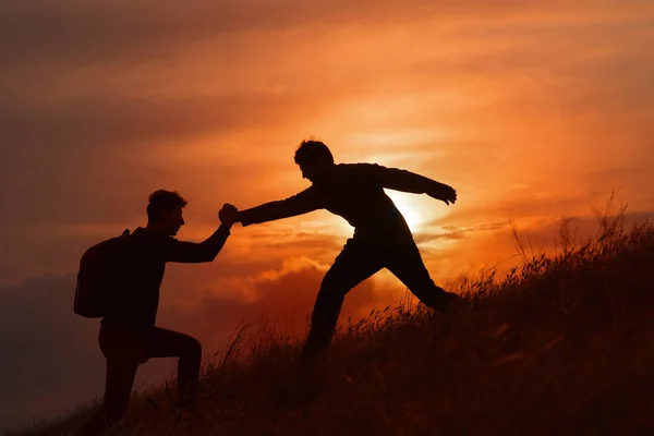 Teamwork couple hiking help each other trust assistance silhouette in mountains, sunset. Teamwork of two men hiker helping each other on top of mountain climbing team, beautiful sunset landscape. — Stock Photo, Image