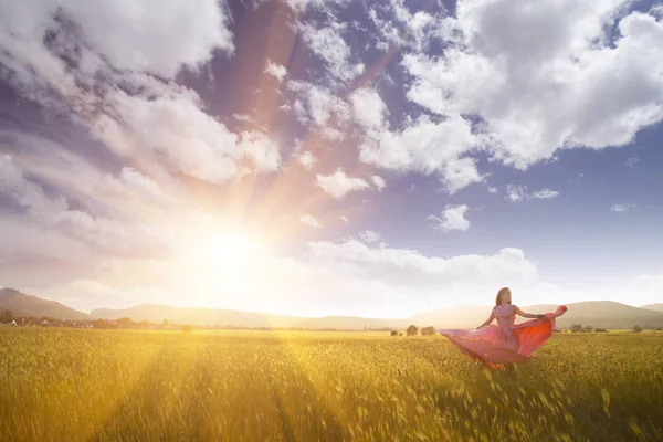 Jovem mulher de pé em um campo de trigo com o nascer do sol no fundo — Fotografia de Stock