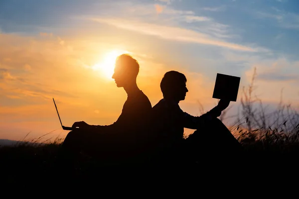 Silhouette of a men with laptop and a book on sunset or sunrise background. —  Fotos de Stock