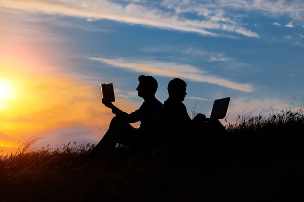 Silhouette of a men with laptop and a book on sunset or sunrise background. — Foto de Stock