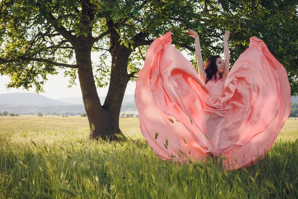Krásy romantická dívka venku. Krásné dospívající Model oblečený v dlouhé růžové šaty na hřišti v Sun světle. Foukání dlouhé vlasy. Na podzim. Záře slunce, sluníčko. Podsvícení. Tónovaný v teplých barvách — Stock fotografie