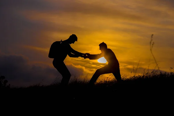 Teamwork koppel wandelen helpen elkaar vertrouwen bijstand silhouet in de bergen, zonsondergang. Teamwork van twee mannen wandelaar elkaar helpen op de top van de berg klimmen team, prachtige zonsondergang landschap. — Stockfoto