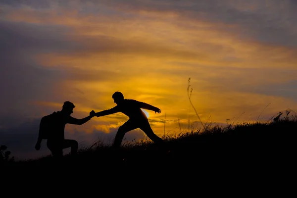 Trabajo en equipo pareja senderismo ayudar a los demás confianza silueta de asistencia en las montañas, puesta del sol. Trabajo en equipo de dos hombres excursionistas ayudándose mutuamente en la parte superior del equipo de escalada, hermoso paisaje al atardecer . —  Fotos de Stock