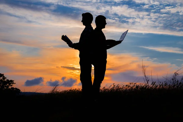 Silhouet van een man met laptop en een boek over zonsondergang of zonsopgang — Stockfoto