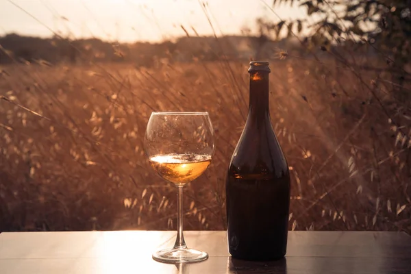 Botella de vino blanco y una copa sobre un fondo de sabana al atardecer —  Fotos de Stock