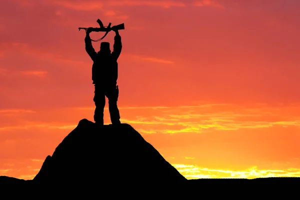 Shot silueta vojáka drží zbraň s malebnou horskou kulisou při západu slunce — Stock fotografie