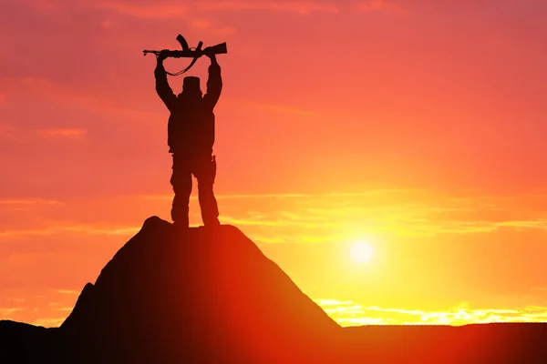 Silhouette shot of a soldier holding a gun with a picturesque mountain backdrop at sunset — Stock Photo, Image