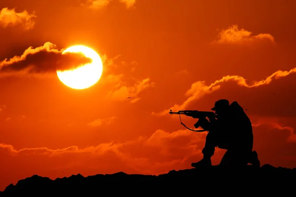 Silhouet shot van een soldaat bezit een pistool met een schilderachtige bergen op de achtergrond bij zonsondergang — Stockfoto