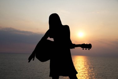 Gitar çalan kızın silueti denizin arka planında ve güzel bir günbatımı