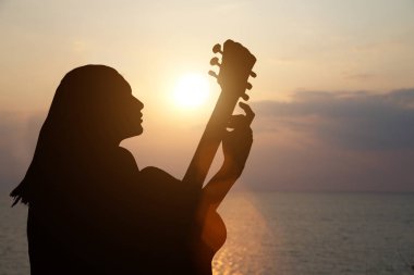 Gitar çalan kızın silueti denizin arka planında ve güzel bir günbatımı