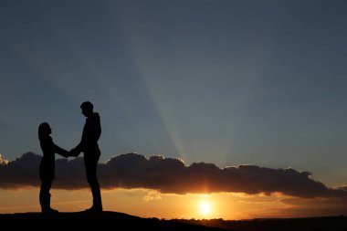 Siluet adam ve kız güzel bir gün batımında el ele tutuşuyorlar.