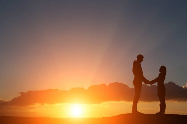 Siluet adam ve kız güzel bir gün batımında el ele tutuşuyorlar.
