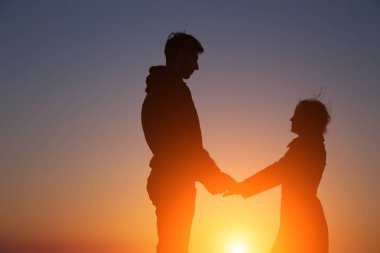 Siluet adam ve kız güzel bir gün batımında el ele tutuşuyorlar.