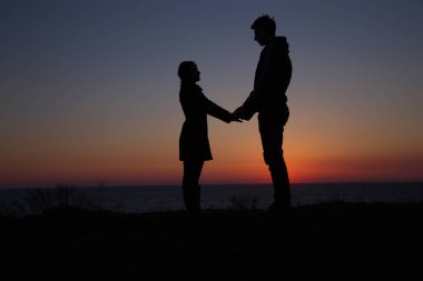 Siluet adam ve kız güzel bir gün batımında el ele tutuşuyorlar.