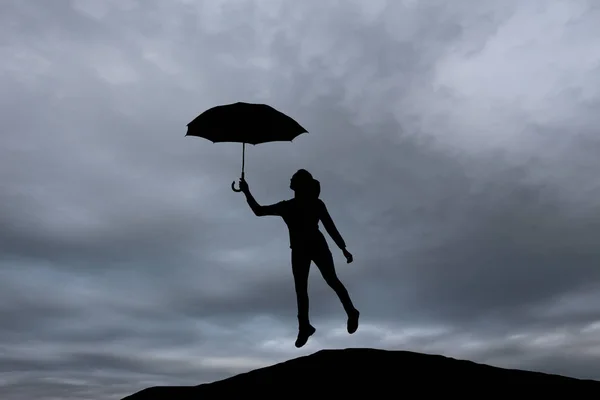 Silhouet van een meisje met een paraplu bij zonsondergang springen — Stockfoto