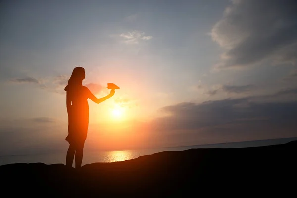 Silhouette of a girl at sunset let a paper plane — Stock Photo, Image