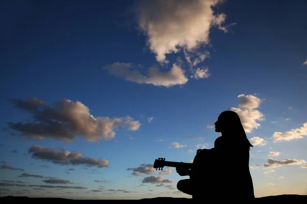 Silhouet van het meisje dat gitaar speelt op de achtergrond van de zee en een prachtige zonsondergang — Stockfoto