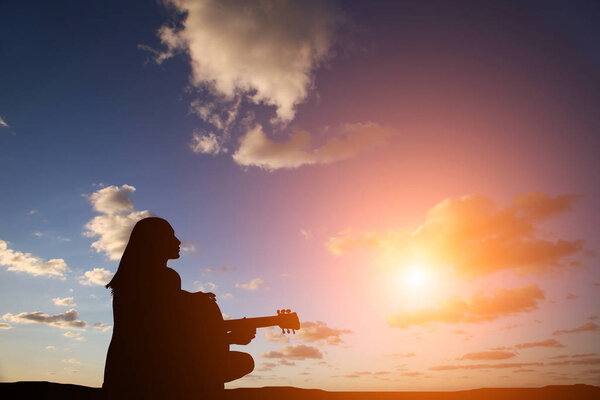 Силуэт девушки, играющей на гитаре на фоне моря и красивого заката
