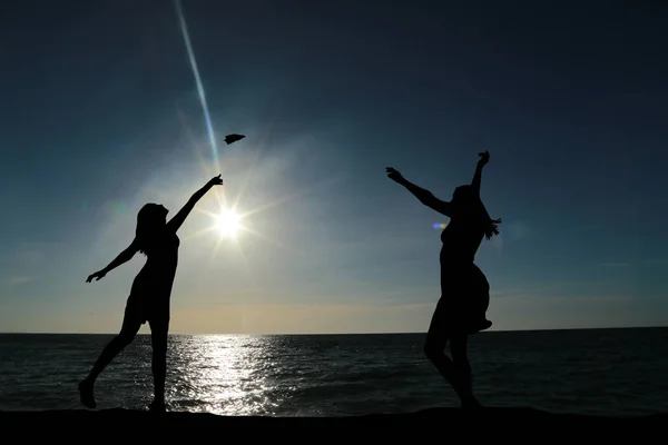 Two girls dancing silhouette against the backdrop of a beautiful sunset and sea — Stock Photo, Image