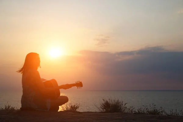 Silhouet van het meisje dat gitaar speelt op de achtergrond van de zee en een prachtige zonsondergang — Stockfoto