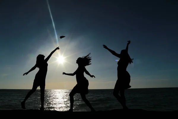 Three girls dancing in silhouette against the background of a beautiful sunset and sea — Stock Photo, Image