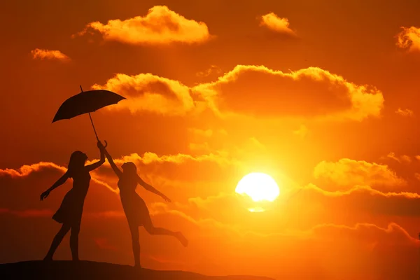 Silhouet twee meisjes op de achtergrond van een prachtige zonsondergang bedrijf paraplu — Stockfoto