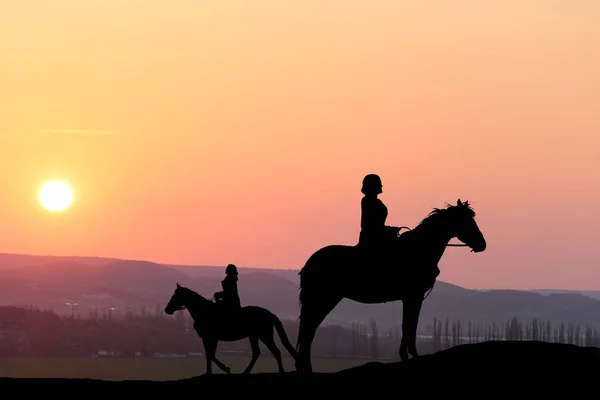 Silhouette two girls ride on a horse on a background of a beautiful sunset — Stock Photo, Image