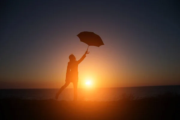 Oamenii pe fundalul unui apus de soare frumos, cu o umbrelă în vedere la mare — Fotografie, imagine de stoc