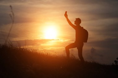 Tepede duran bir adam güzel bir günbatımının arka planındaki bağlantıya bakıyor.