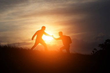 Erkek ve dişi yürüyüşçüler dağ uçurumuna tırmanıyor ve içlerinden biri yardım eli uzatıyor. Yardım eden insanlar ve takım çalışması konsepti.