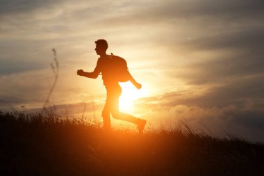 İnsan güzel bir gün batımına karşı bir tepede koşar.