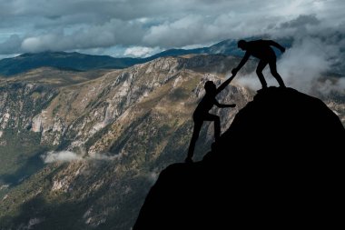 Male and female hikers climbing up mountain cliff and one of them giving helping hand. People helping and, team work concept. clipart