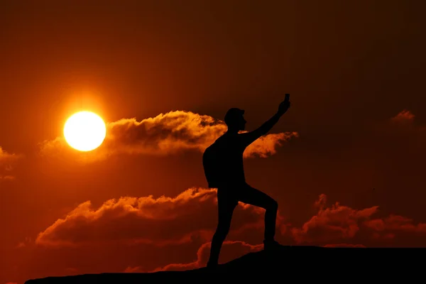 Ein Mann, der auf einem Hügel steht und auf den Hintergrund eines wunderschönen Sonnenuntergangs blickt — Stockfoto