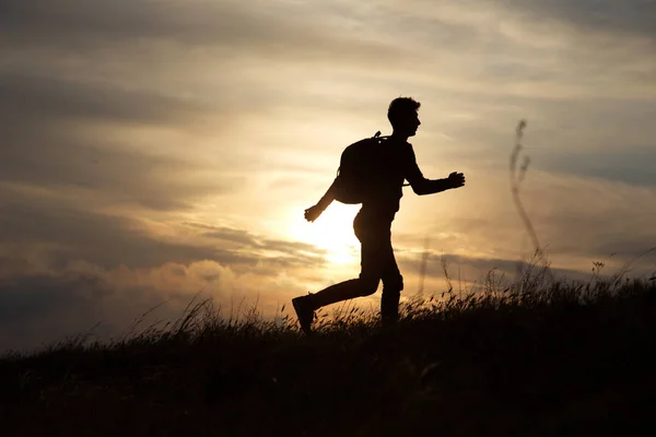 L'uomo corre direttamente su una collina contro un bel tramonto — Foto Stock