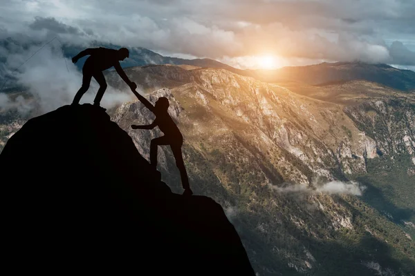 Male and female hikers climbing up mountain cliff and one of them giving helping hand. People helping and, team work concept. — Stock Photo, Image