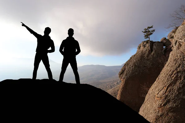 Silueta de dos hombres de pie sobre una roca mirando a la distancia — Foto de Stock