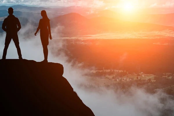 Silueta del hombre y la mujer en la cima de la montaña sobre un hermoso fondo —  Fotos de Stock