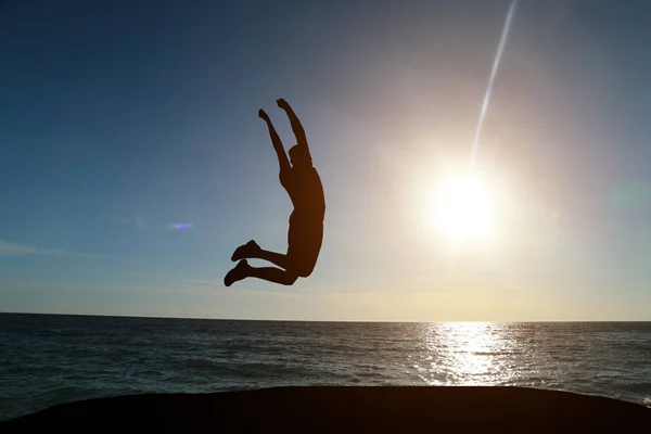 Silhueta de um homem pulando em um fundo do mar e um belo pôr do sol — Fotografia de Stock