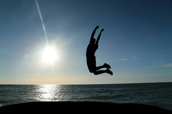 Güzel bir gün batımı ve deniz bir arka plan üzerinde atlama bir adam silüeti — Stok fotoğraf
