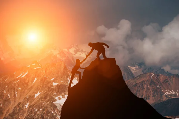 Male and female hikers climbing up mountain cliff and one of them giving helping hand. People helping and, team work concept. Royalty Free Stock Photos