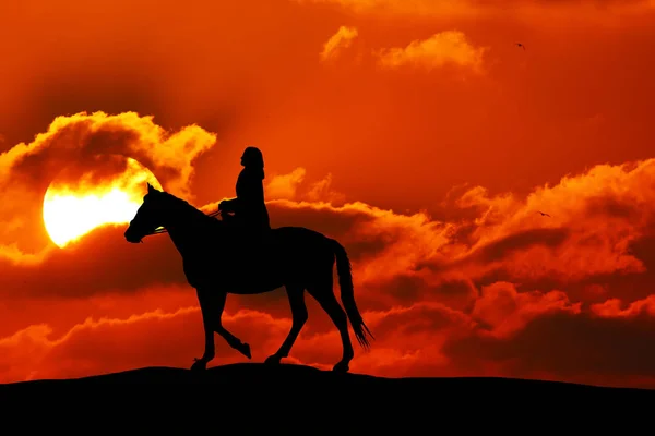 Silhouette or woman and horse running across horizon as the sun goes down. — Stock Photo, Image