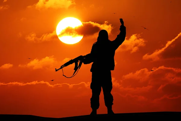 Silhueta de soldado militar ou oficial com armas ao pôr do sol. tiro, segurando arma, céu colorido, montanha, fundo — Fotografia de Stock