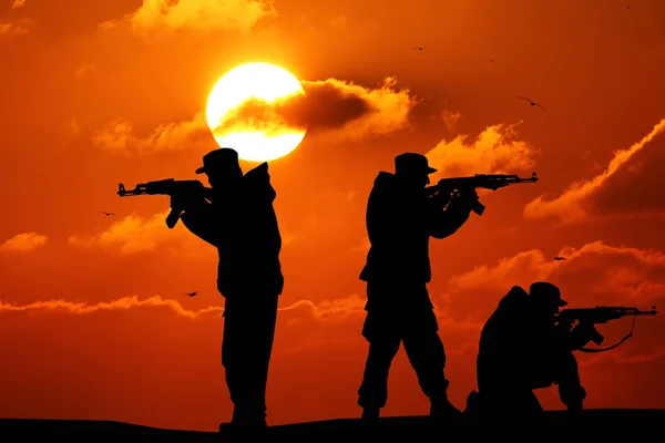 Silueta de militar tres soldado o oficial con armas al atardecer. disparo, pistola de mano, cielo colorido, montaña, fondo, equipo — Foto de Stock