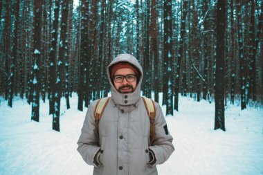 Genç adam kışın karlı ormanda duruyor.