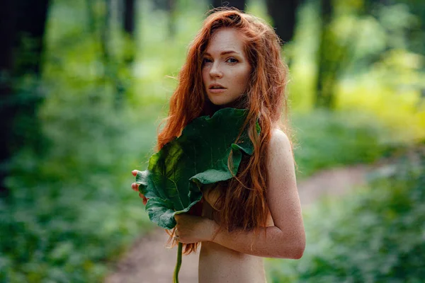 A young ginger woman stand in the green forest.