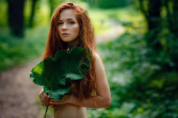 Mladá zrzavá žena stojí v zeleném lese. — Stock fotografie