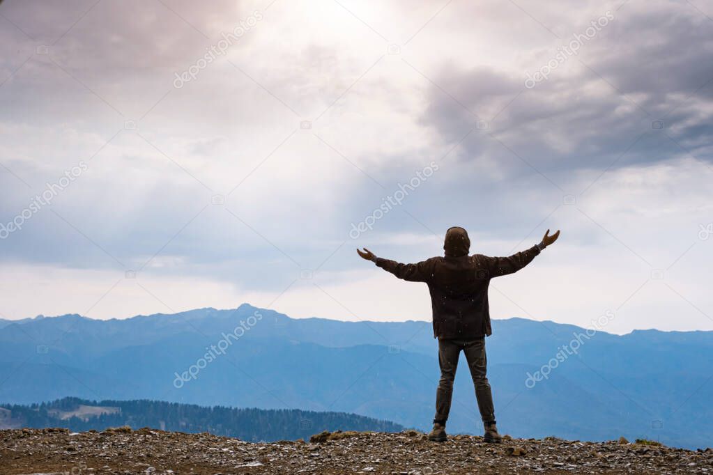 Landscape with silhouette of a standing happy man and raised-up arms on the mountain peak on the background of cloudy sky. autumn rain in the mountains