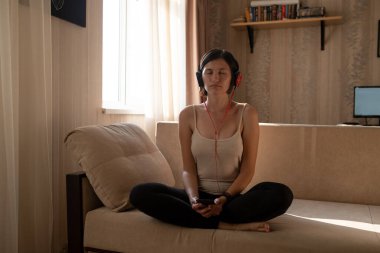 Evde izole ve rahatlatıcı genç bir kadın: Coronavirus önleme için sosyal medya kampanyasında evde kalın. Akıllı telefon, meditasyon ve rahatlama uygulaması ile meditasyon