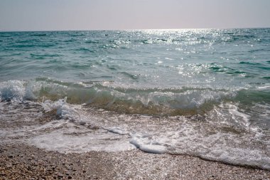 İlkbaharda öğle vakti güzel deniz, berrak su, kayalık sahil. Sessiz dalgalar gün ortası güneşiyle aydınlanır.