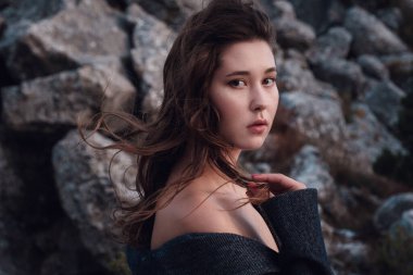 Gri paltolu güzel bir Asyalı kadın iç çamaşırının üzerinde, dağların manzarasının tadını çıkarıyor. Yüksek tepeler ve mavi deniz. Özgürlük, seyahat ve macera fikri ve konsepti